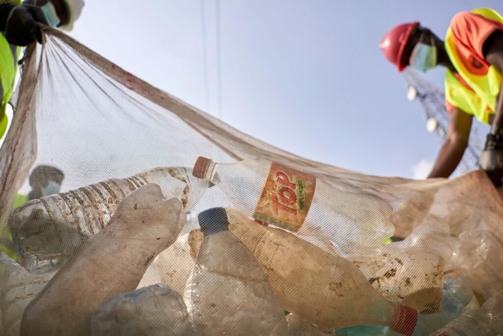 Two workers gather plastic bottles and trash in a net to combat pollution.